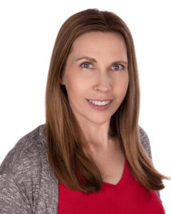 Professional Headshot of a woman with long hair wearing a red v-neck shirt and grey cardigan.