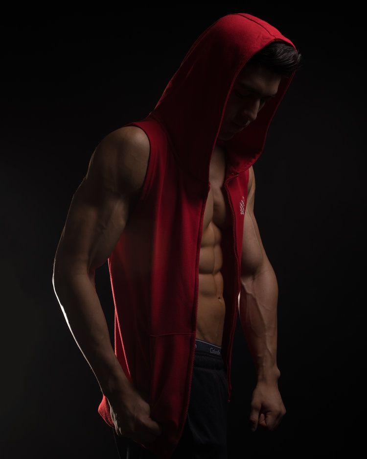 Fitness photograph of an athletic man wearing a sleeveless red hoodie.